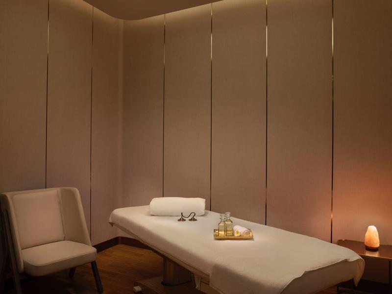 Einfach eingerichteter Massageraum mit Behandlungsliege, Stuhl, Handtüchern und warmem Licht.