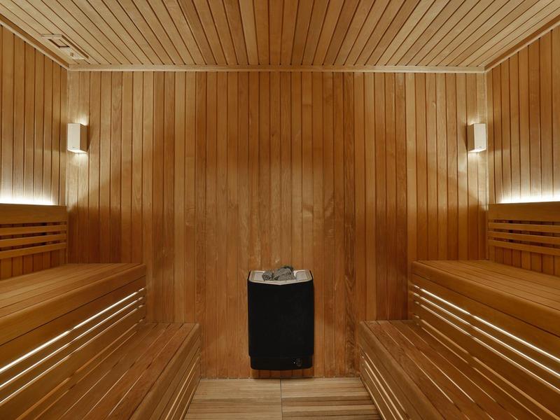 Sauna mit holzverkleideten Wänden, Sitzbänken und zentralem Ofen, warme Beleuchtung.