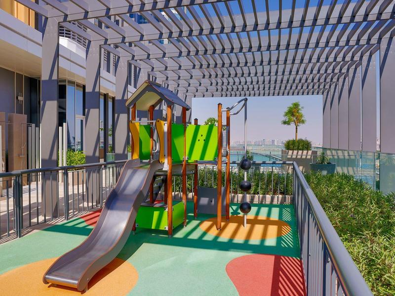 Kinderspielplatz auf einer Dachterrasse mit Rutsche, Schaukeln und buntem Bodenbelag unter Pergola.