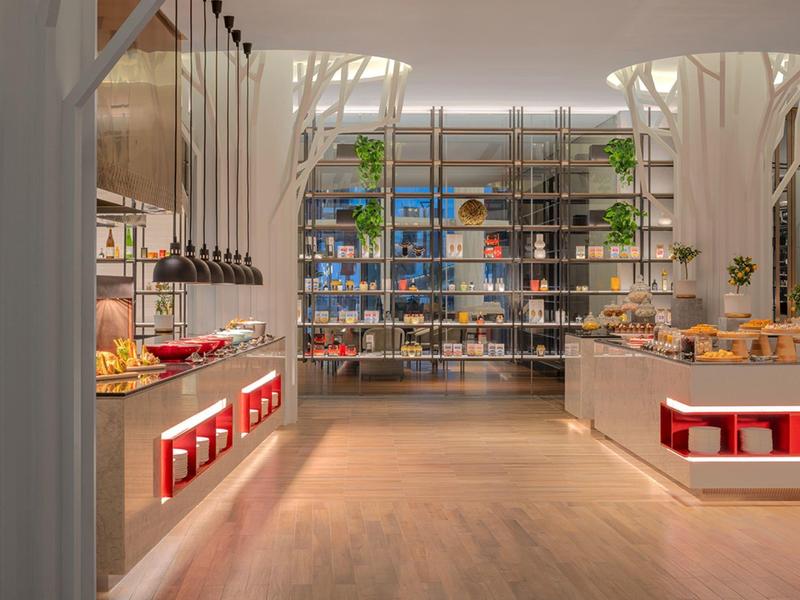 Moderní, světlá bufetová restaurace s dlouhou dřevěnou podlahou a otevřenými regály.