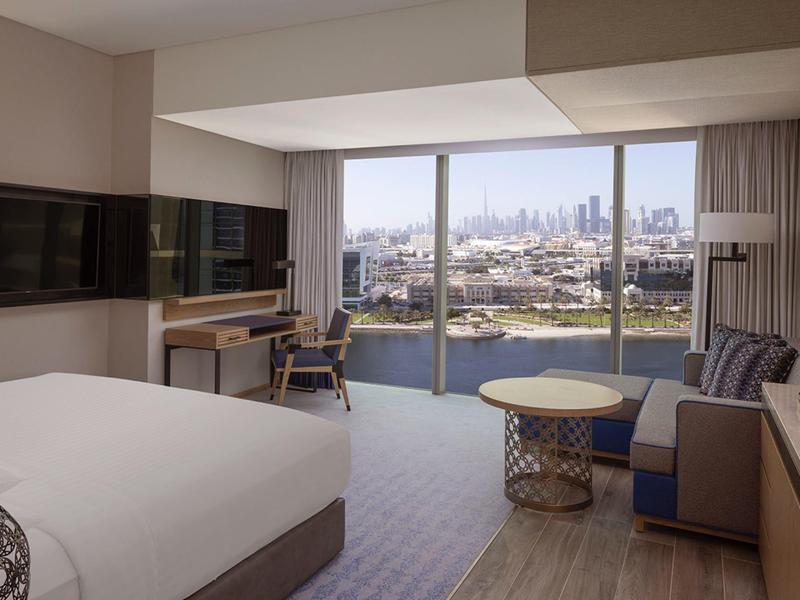 Moderní hotelový pokoj s postelí, posezením a oknem s výhledem na město.