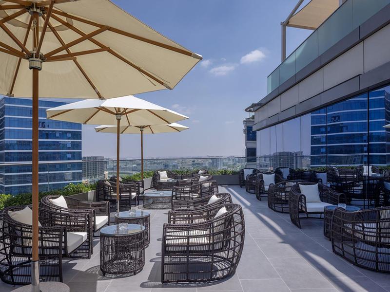 Moderní hotelová střešní terasa s posezením, slunečníky a výhledem na město.