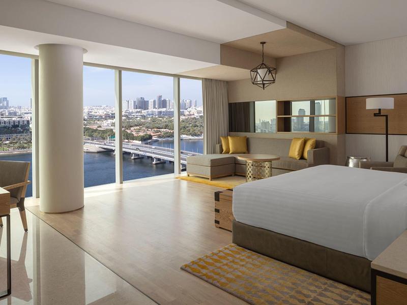 Světý hotelový pokoj s manželskou postelí, posezením a panoramatickým výhledem na vodu a město.