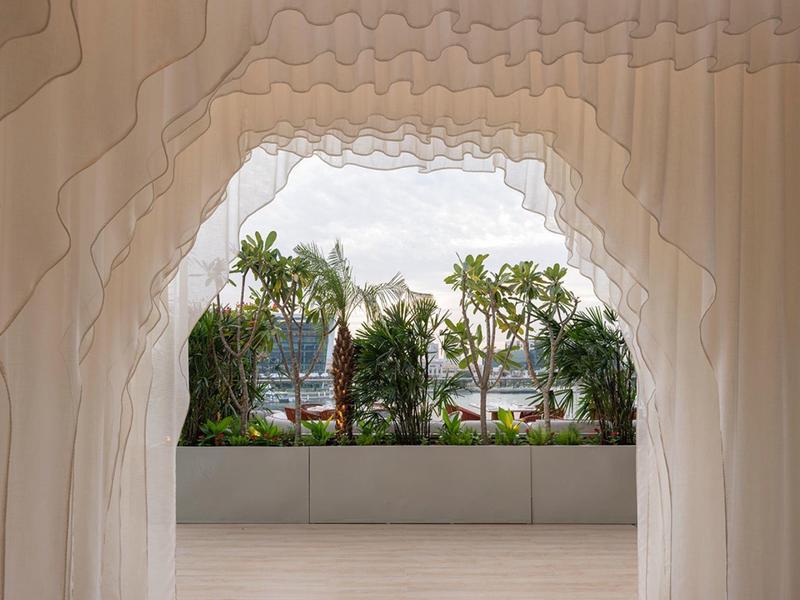 Výhled skrz architektonický otvor na tropické rostliny a oblačnou oblohu.