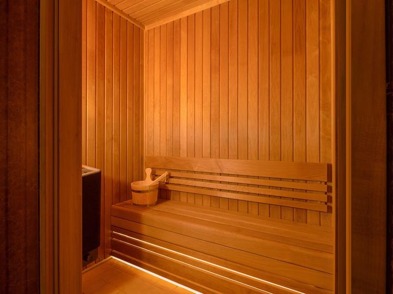 Teplá, světlá sauna s dřevěnými lavicemi a saunovým kamenem