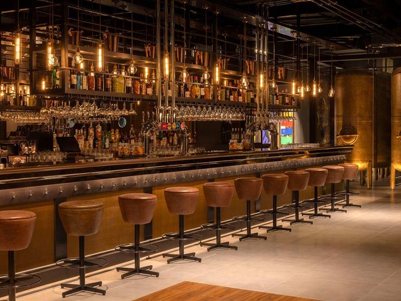 Moderní hotelový bar s dlouhými barovými židlemi a teplým osvětlením.