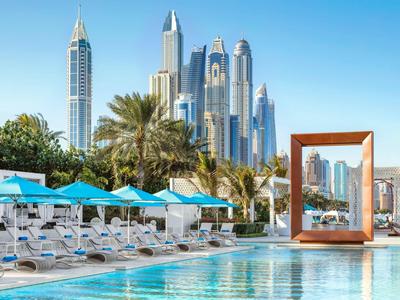 Luxe zwembadgebied met ligstoelen en uitzicht op moderne wolkenkrabbers in een zonnige stad.