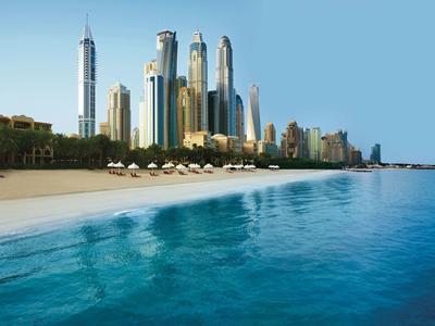 Helder blauw water met een zandstrand en wolkenkrabbers op de achtergrond bij zonnig weer.