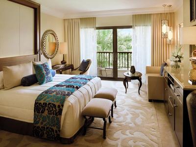 Elegant hotelkamer met groot bed, balkon en stijlvolle meubels in warme kleuren.