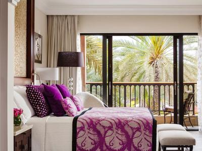 Elegant hotelkamer met paarse dekbed en kussens, grote ramen en uitzicht op palmbomen.