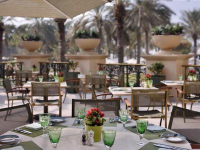 Buitenterras van een restaurant met tafels, groene glazen en bloemen als decoratie bij zonnig weer.