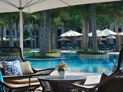 Area piscina con lettini, tavolo e ombrellone in un contesto alberghiero tropicale.