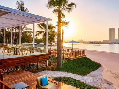 Strandresort met houten balkon, palmbomen en zonsondergang boven kalm water
