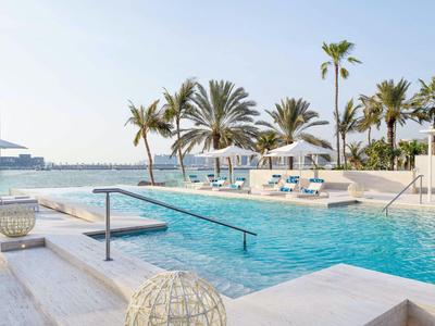 Piscina moderna dell'hotel con palme e vista sul mare in una giornata di sole.
