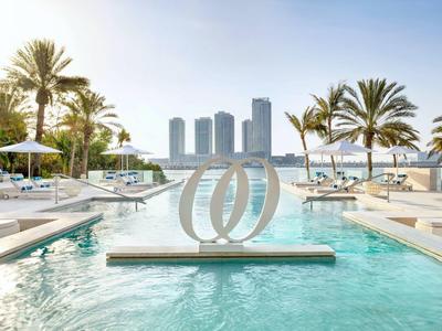 Modern buitenzwembad met palmbomen, ligstoelen en stadszicht onder heldere hemel.