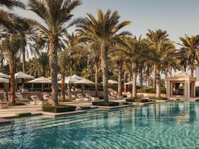 Area piscina di lusso con ombrelloni e palme in un resort alberghiero sotto un cielo sereno.
