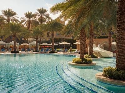 Ein tropischer Hotelpool mit Palmen, Liegestühlen und Sonnenschirmen in der Abenddämmerung.