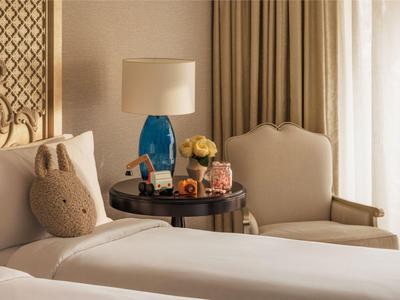 Hotelkamer met twee bedden, een nachtkastje met een blauwe lamp en een fauteuil bij het raam.