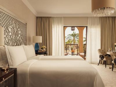 Camera d'hotel luminosa con letto matrimoniale, pannello decorativo e balcone con piante.