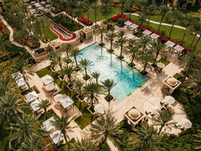 Vista dall'alto di una piscina rettangolare con lettini e palme in un giardino tropicale di un hotel.