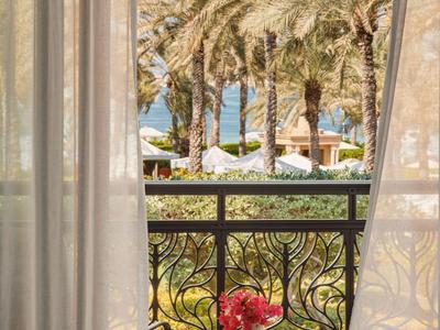 Balkon met uitzicht op palmbomen, een zwembad en witte parasols, met tafel en stoelen.