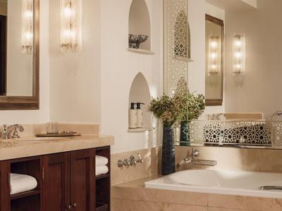 Lichte badkamer met badkuip, spiegels, houten kasten en decoratieve wandniches.