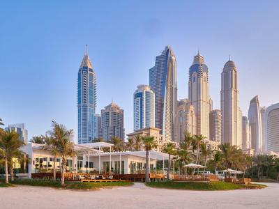 Moderne wolkenkrabbers en luxe woningen aan het strand met palmbomen en blauwe lucht.
