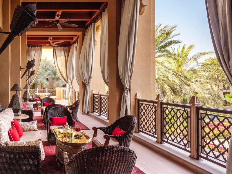 Gezellig balkon met rotan stoelen en gordijnen, uitzicht op palmbomen en blauwe lucht.