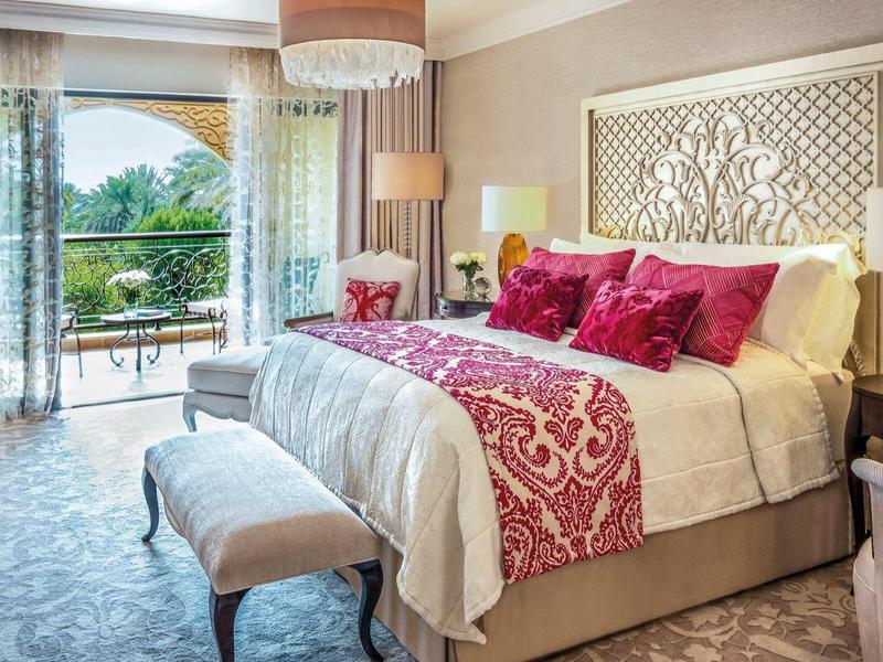 Lichte hotelkamer met groot bed, rode kussens en balkon met uitzicht op bergen.