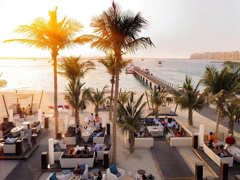 Strandresort met zitgedeeltes en palmbomen aan zee bij zonsondergang