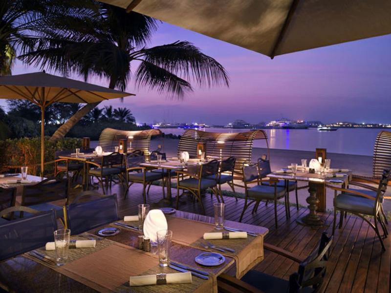 Verlichte buitenterras van restaurant met uitzicht op de kust bij schemering.