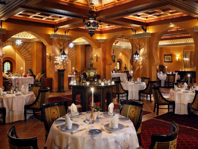 Elegant en warm verlicht restaurant met ronde gedekte tafels en houten lambrisering.