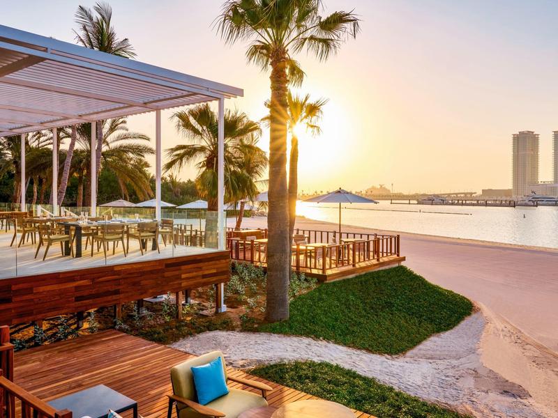 Strandresort met houten balkon, palmbomen en zonsondergang boven kalm water