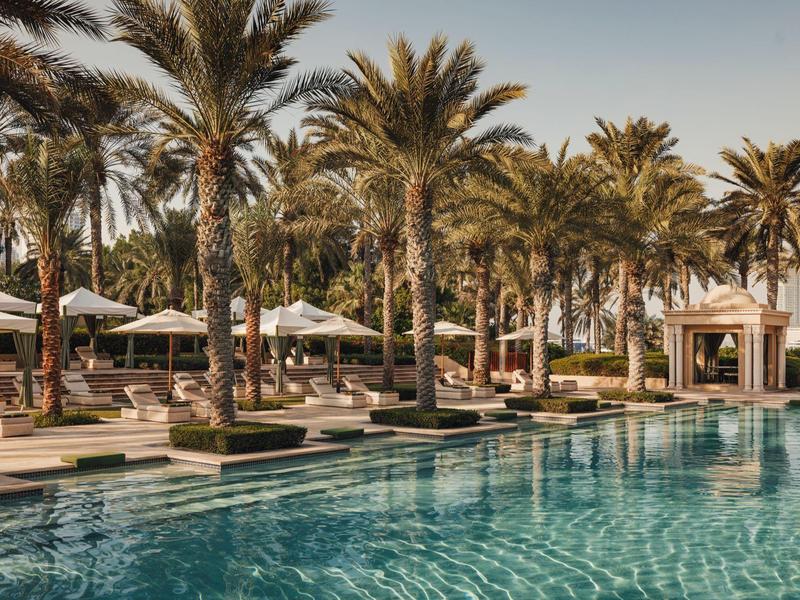 Modern buitenzwembad met ligbedden en palmbomen onder een heldere lucht.