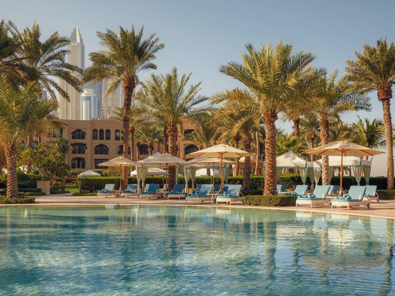 Een hotelzwembad met ligstoelen en parasols omgeven door palmbomen.