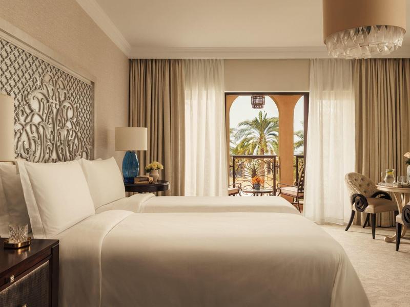 Elegante hotelkamer met groot bed, decoratief wandpaneel en balkonzicht met palmboom.