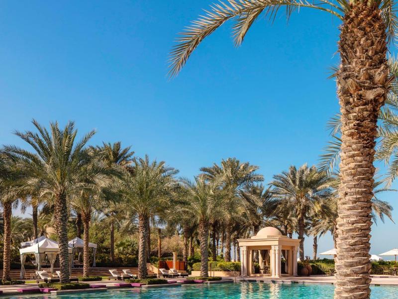 Een zwembad met palmbomen en ligstoelen onder een heldere blauwe hemel in een tropische vakantiebestemming.