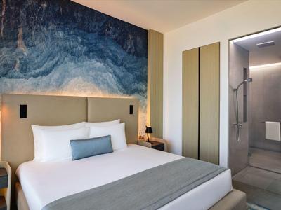 Moderne hotelkamer met groot bed, abstracte muurschildering en open badkamer met douche.