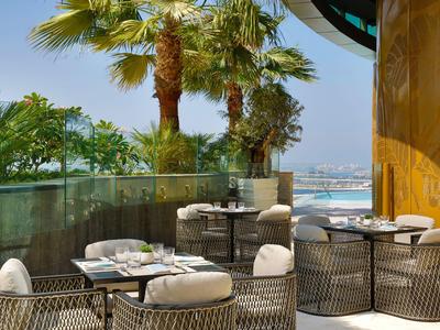 Terras met tafels en stoelen, palmbomen en zeezicht op een zonnige dag