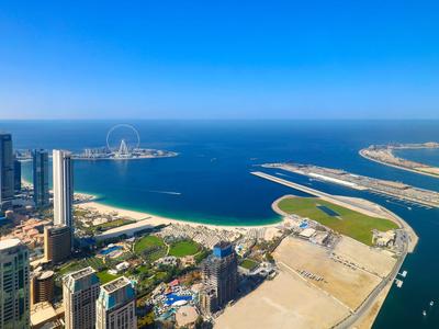 Luchtfoto van een kuststad met wolkenkrabbers, jachthaven en heldere blauwe lucht.