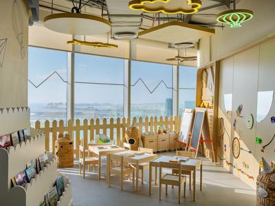 Lichte kinderspeelruimte met houten tafels, stoelen en groot raam met uitzicht op zee.