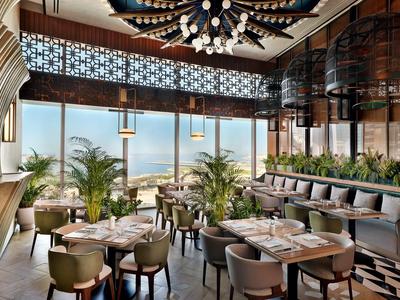 Elegant restaurant met panoramische ramen, planten en moderne verlichting met uitzicht op zee.