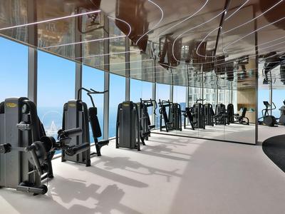 Moderne fitnessruimte met krachtapparatuur en groot raam met uitzicht op zee.