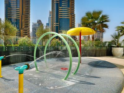 Water-speelplaats voor kinderen met bogen en sproeiers in een stedelijke omgeving met hoge gebouwen.