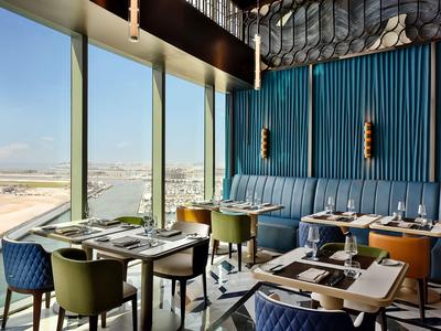 Modern restaurant met grote ramen met uitzicht op de stad, stijlvolle meubels en gedempte kleuren.