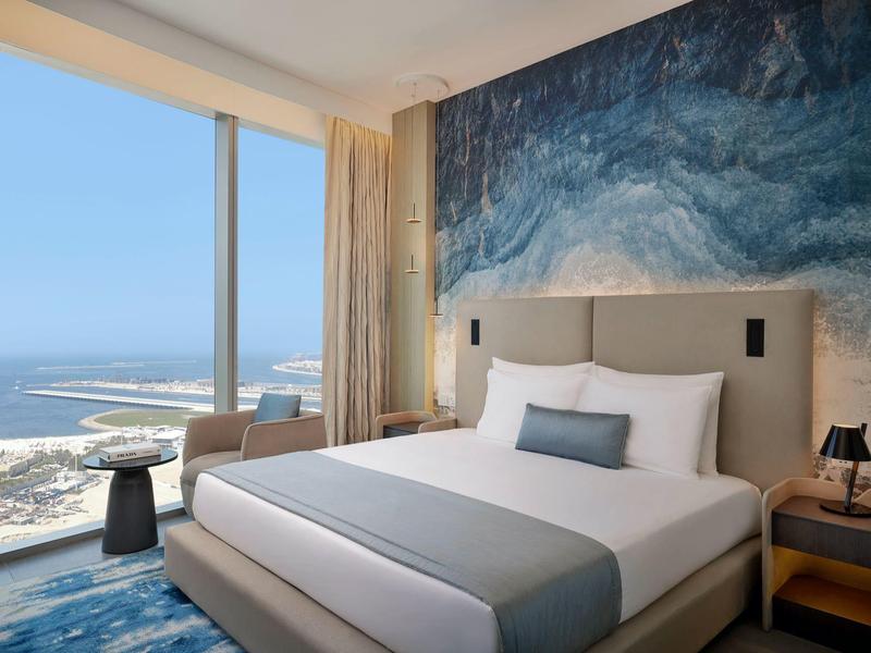 Modern hotelkamer met groot bed en zeezicht door vloervullende ramen.