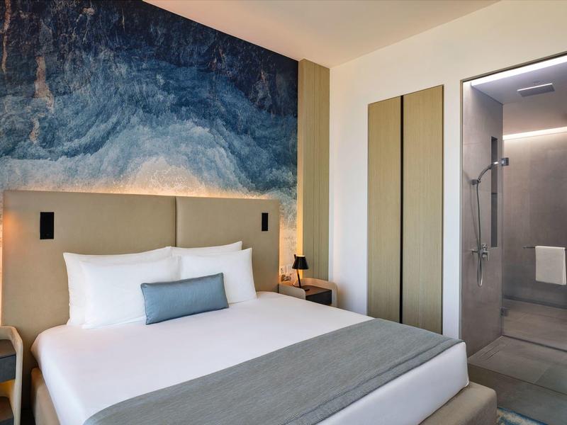 Moderne hotelkamer met groot bed, abstracte muurschildering en open badkamer met douche.