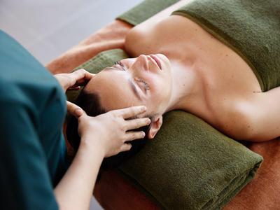 Entspannte Frau erhält Gesichtsmassage auf einer Massageliege mit grünem Handtuch.