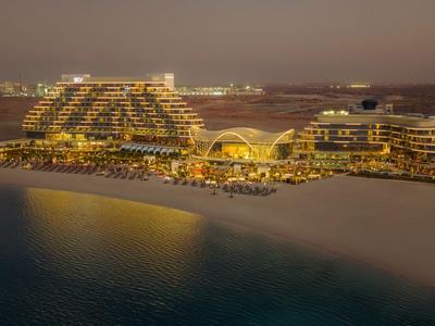 Beleuchtetes Luxushotel am Strand bei Nacht mit Blick auf das Meer und die umliegende Stadt.