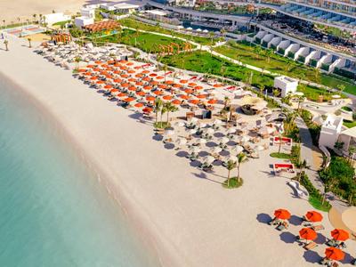 Weißer Sandstrand mit Sonnenschirmen und Liegen neben einem modernen Hotelgebäude.